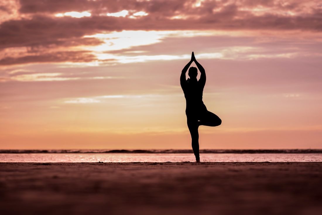 Christine Raab macht die Yogapose Baum am Strand in Holland Silouettenbild im Sonnenuntergang orange