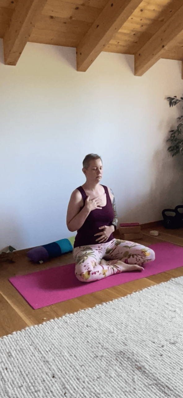 Christine raab sitzt auf einer rosa Yogamatte und zeigt Yogaübungen für schlechte Tage. Atmen, entspannen, Mantra hören.