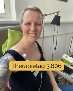 Christine Raab schaut lächelnd in die Kamera. Im Hintergrund sieht man ein medizinisches Zimmer, sie hat eine grüne Decke hinter dem Kopf und eine Portnadel steckt oben neben dem Schlüsselbein. Der Text auf dem Bild sagt: Therapietag 3.806